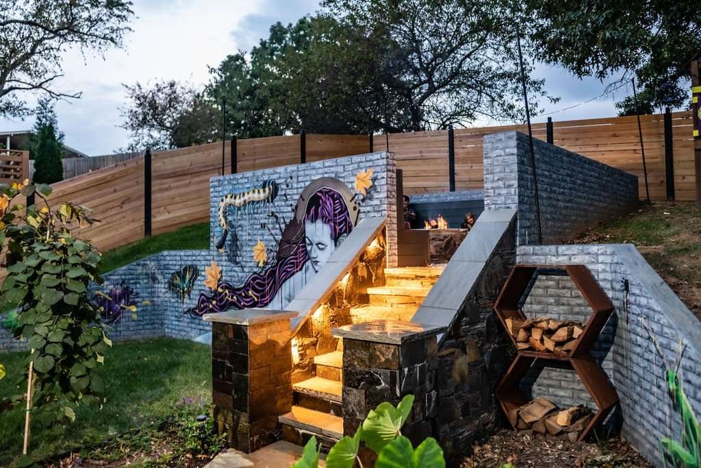 Outdoor hardscaping featuring a stone staircase with illuminated steps, vibrant mural, and wooden fencing, enhancing a backyard space for family gatherings and relaxation.