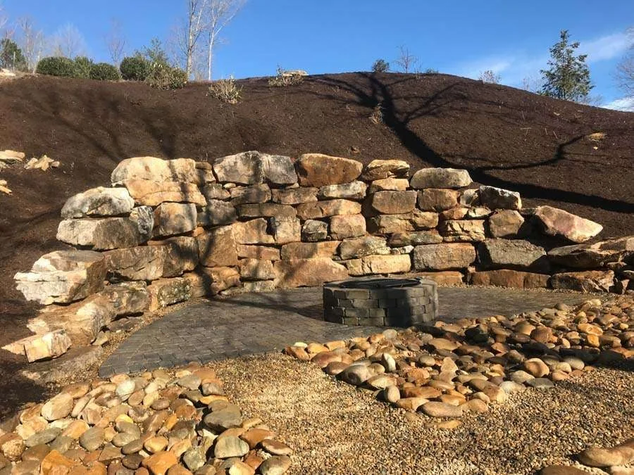 Curved natural-stone landscape wall beside a paved fire-pit area