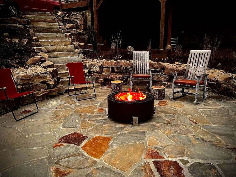 Laughter Family Hardscapes Hardscaping Services Buncombe County NC -03 The image depicts a lit fireplace and a completed hardscape design with pavers and retaining walls.