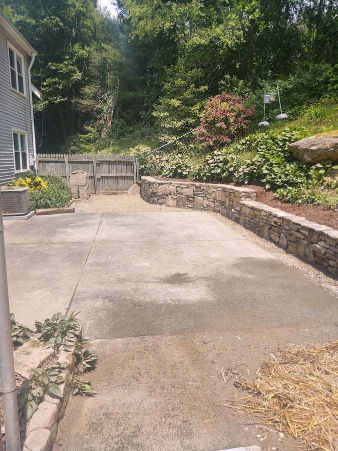 Laughter Family Hardscapes Hardscaping Services Buncombe County NC -12 The image depicts a backyard concrete patio and a aesthetically pleasing and structurally sound stone retaining wall.